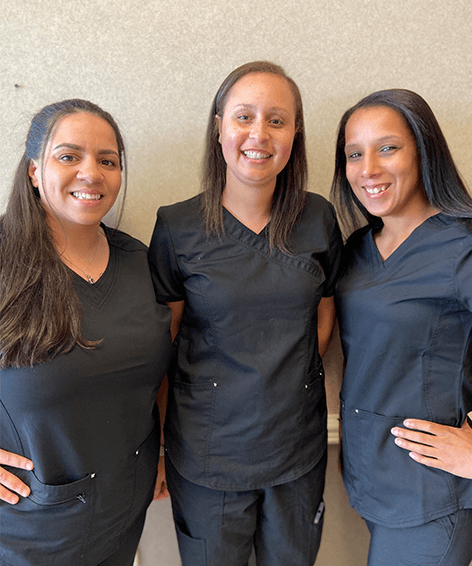 three female staff of Associates in Nephrology in scrubs smiling at the camera