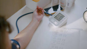 Asian Senior woman sitting on a chair and check blood pressure gauge and heart rate using digital sphygmomanometer in living room at home at day time. Mature senior doing medical examining in a day time. Medium shot