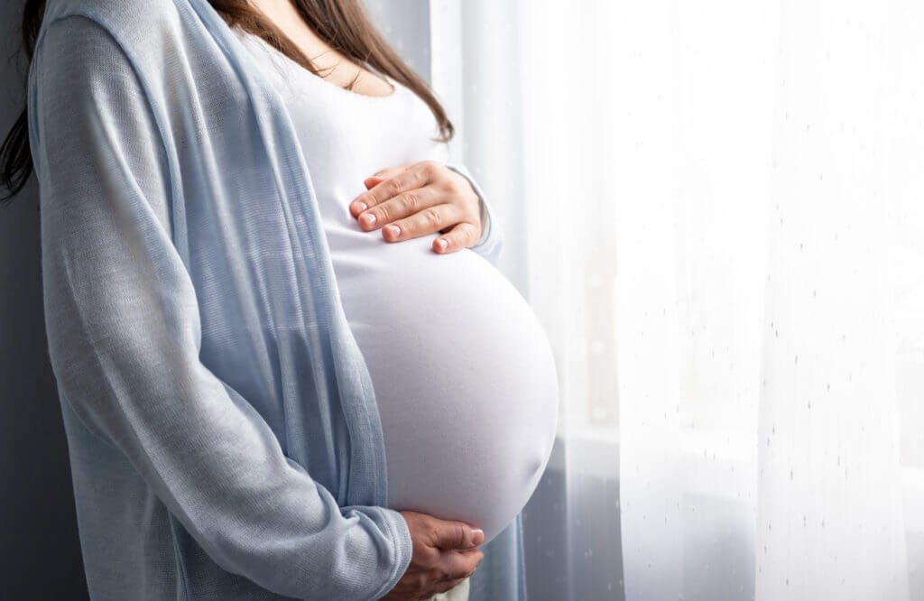 Image of pregnant woman holding pregnant belly in hands due to proteinuria pain.
