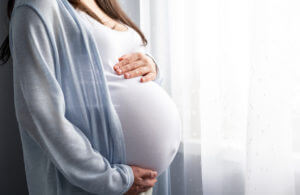 Image of pregnant woman holding pregnant belly in hands due to proteinuria pain.